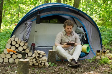 Backpacker açık havada bir tablet kullanır. Bahar yeşil orman.