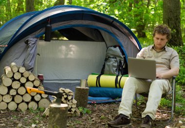 Bir laptop bir çadır kampında açık havada çalışan bir erkeğin.