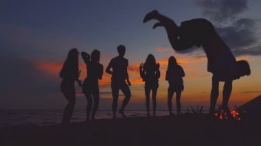 Plaj partisi. Ters takla atarak yapan genç erkek. Adam arkadaşlar siluetleri.