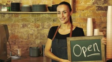 Bir kahve dükkanı işçi ve açık bir işaret tutan müşteri görünüyor.