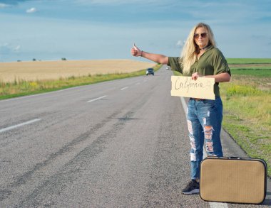 Yaz aylarında yolda otostop sırasında işaret tutan sarışın.