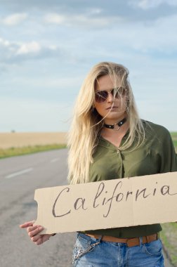 Yaz aylarında yolda otostop sırasında işaret tutan ciddi sarışın.