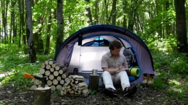 Backpacker bir defterde açık havada notlar alır. Doğada kamp.