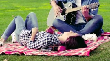 Mutlu çift aşık yeşil çimenlerin üzerine iyi vakit geçiriyor. Adam gitar çalıyor.