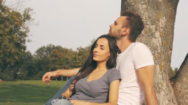 Mutlu çift oturma parkta ağaç yakınındaki ve sarılma.