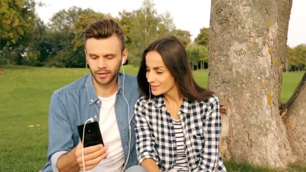 Pareja Feliz Tumbada Bajo Árbol Escuchando Música — Vídeos de Stock