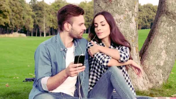 Pareja Feliz Tumbada Bajo Árbol Escuchando Música — Vídeos de Stock