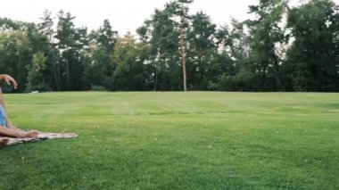 Baba anne ve küçük kızı parkta çimenlerin üzerinde oturuyor.