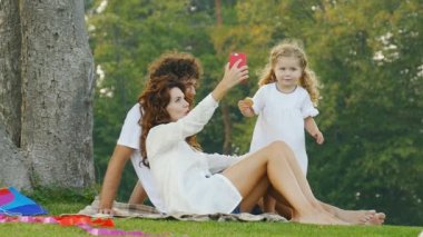 Dışarıda, parkta mutlu bir aile var. Eğlenmek ve aile selfie'leri çekmek. Yavaş çekim video.