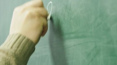 Okutman tahtaya tebeşirle yazıyor. Okutman elin yakın plan çekimi..