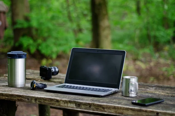 Dışarıdaki ahşap bir masada dizüstü bilgisayar, kamera, kahve ve akıllı telefonun yakın plan fotoğrafı..