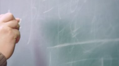 Okutman tahtaya tebeşirle yazıyor. Okutman elin yakın plan çekimi..