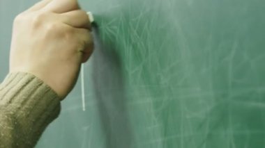 Okutman tahtaya tebeşirle yazıyor. Okutman elin yakın plan çekimi..