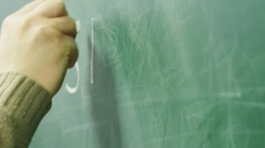 Okutman tahtaya tebeşirle yazıyor. Okutman elin yakın plan çekimi..