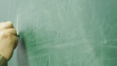 Okutman tahtaya tebeşirle yazıyor. Okutman elin yakın plan çekimi..