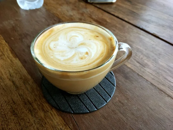 Gorąca kawa cappuccino w przezroczystej szklance na drewnianej podłodze. — Zdjęcie stockowe