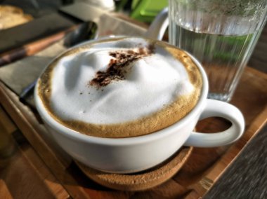 Beyaz fincan üzerinde Sabah bulanık Kahve latte, ahşap masada bir kahve dükkanı kafe.