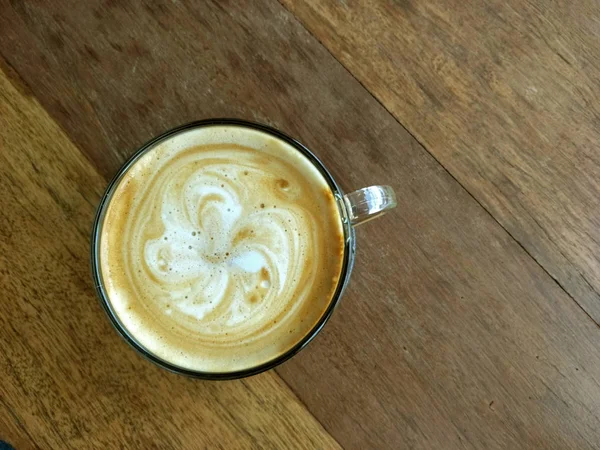 Café caliente cappuccino en un vaso transparente sobre un suelo de madera . —  Fotos de Stock