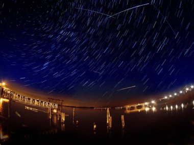 Gökyüzünü geçen birden fazla meteor çizgileri ile Perseid meteor yağmuru, su üzerinde uzun pozlama tarafından oluşturulan yıldız parkurları
