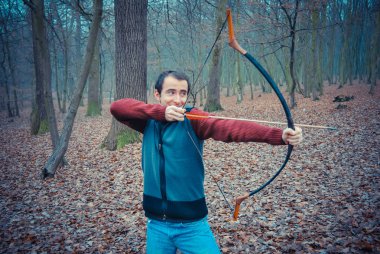 Genç adam sonbahar ormanında yaydan ateş ediyor.