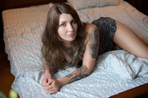 Plus size sexy model with tattoos lies on a large wooden bed