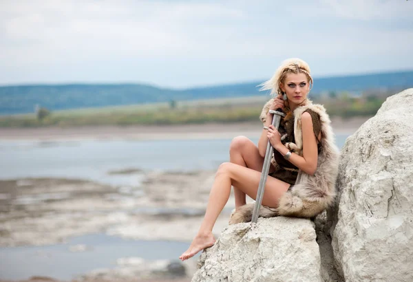 European Woman a warrior in Scandinavian Viking style dressed in a wolf\'s hide sitting with a sword in his hands on the edge of a cliff.
