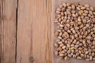 Kırık ahşap bir masanın üzerindeki el işi parşömende kızarmış tuzlu şam fıstığı serpiştirilmiş..