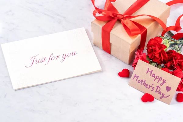 Maj mors dag handgjord presentbox önskar fotografi - vackra blommande nejlikor med rött band bow box isolerade på moderna marmor skrivbord, närbild, kopiera utrymme, håna upp — Stockfoto