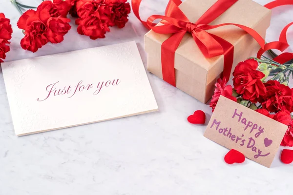 Mayo madres día hecho a mano regalos cuadro desea fotografía - Hermosos claveles en flor con caja de lazo de cinta roja aislado en el escritorio de mármol moderno, primer plano, espacio para copiar, maqueta — Foto de Stock