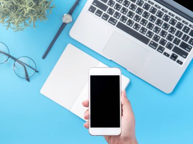 Bir kadın minimal mavi masa ile izole bir akıllı telefon tutuyor, online alışveriş ödeme kavramı, evde internet çalışması, e-ticaret, kopya alanı, düz yatıyordu, üst görünüm, alay
