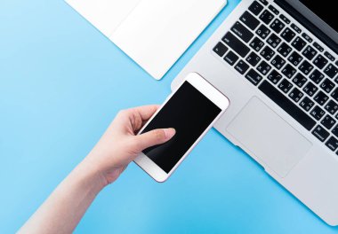 Bir kadın minimal mavi masa ile izole bir akıllı telefon tutuyor, online alışveriş ödeme kavramı, evde internet çalışması, e-ticaret, kopya alanı, düz yatıyordu, üst görünüm, alay