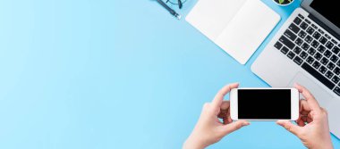 Bir kadın minimal mavi masa ile izole bir akıllı telefon tutuyor, online alışveriş ödeme kavramı, evde internet çalışması, e-ticaret, kopya alanı, düz yatıyordu, üst görünüm, alay