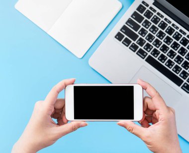 Bir kadın minimal mavi masa ile izole bir akıllı telefon tutuyor, online alışveriş ödeme kavramı, evde internet çalışması, e-ticaret, kopya alanı, düz yatıyordu, üst görünüm, alay