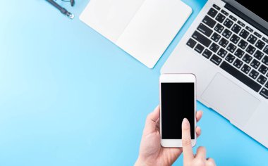 Bir kadın minimal mavi masa ile izole bir akıllı telefon tutuyor, online alışveriş ödeme kavramı, evde internet çalışması, e-ticaret, kopya alanı, düz yatıyordu, üst görünüm, alay