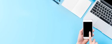 Bir kadın minimal mavi masa ile izole bir akıllı telefon tutuyor, online alışveriş ödeme kavramı, evde internet çalışması, e-ticaret, kopya alanı, düz yatıyordu, üst görünüm, alay