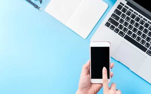 A woman is holding a smartphone isolated with a minimal blue desk, concept of online shopping payment, internet work at home, e-commerce, copy space, flat lay, top view, mock up