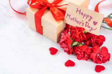 El yapımı giftbox fotoğrafçılık - modern mermer masasında izole kırmızı şerit yay kutusuyla güzel çiçek açan karanfil dilek Mayıs Anneler günü yakın çekim, uzay kopyalayın, yukarı alay