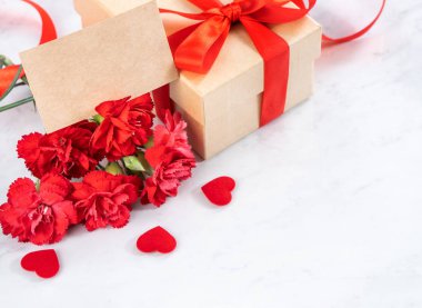El yapımı giftbox fotoğrafçılık - modern mermer masasında izole kırmızı şerit yay kutusuyla güzel çiçek açan karanfil dilek Mayıs Anneler günü yakın çekim, uzay kopyalayın, yukarı alay