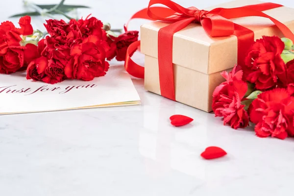 May mothers day handmade giftbox wishes photography - Beautiful blooming carnations with red ribbon bow box isolated on modern marble desk, close up, copy space, mock up — Stock Photo, Image