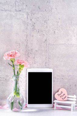 Masanın üzerinde duvar yanında fotoğraf çerçevesi olarak çiçekkaranfil ve tablet ile ev dekorasyonu - Yakın, kopya alanı, mock up, güzel anneler günü kavramı.