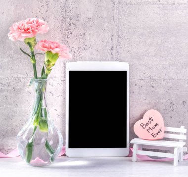 Masanın üzerinde duvar yanında fotoğraf çerçevesi olarak çiçekkaranfil ve tablet ile ev dekorasyonu - Yakın, kopya alanı, mock up, güzel anneler günü kavramı.