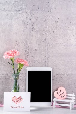 Masanın üzerinde duvar yanında fotoğraf çerçevesi olarak çiçekkaranfil ve tablet ile ev dekorasyonu - Yakın, kopya alanı, mock up, güzel anneler günü kavramı.