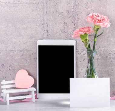 Masanın üzerinde duvar yanında fotoğraf çerçevesi olarak çiçekkaranfil ve tablet ile ev dekorasyonu - Yakın, kopya alanı, mock up, güzel anneler günü kavramı.