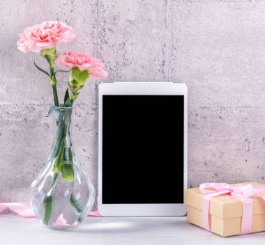 Masanın üzerinde duvar yanında fotoğraf çerçevesi olarak çiçekkaranfil ve tablet ile ev dekorasyonu - Yakın, kopya alanı, mock up, güzel anneler günü kavramı.