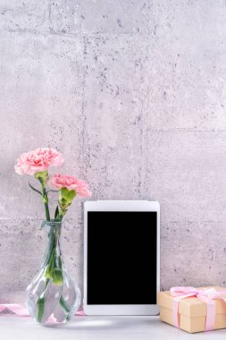 Masanın üzerinde duvar yanında fotoğraf çerçevesi olarak çiçekkaranfil ve tablet ile ev dekorasyonu - Yakın, kopya alanı, mock up, güzel anneler günü kavramı.