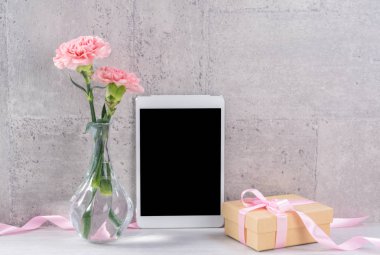 Masanın üzerinde duvar yanında fotoğraf çerçevesi olarak çiçekkaranfil ve tablet ile ev dekorasyonu - Yakın, kopya alanı, mock up, güzel anneler günü kavramı.