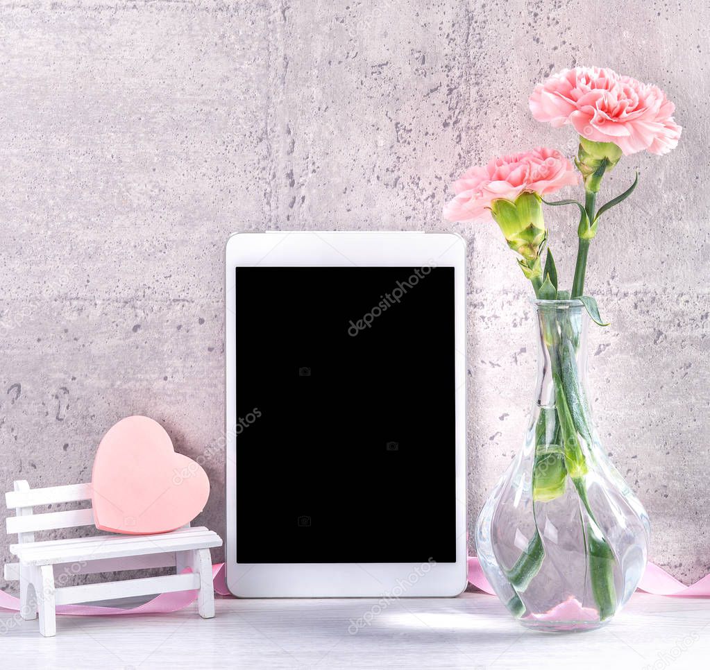 Home decor with blooming carnation and tablet as photo frame beside wall on the table - Close up, copy space, mock up, beautiful mothers day concept.