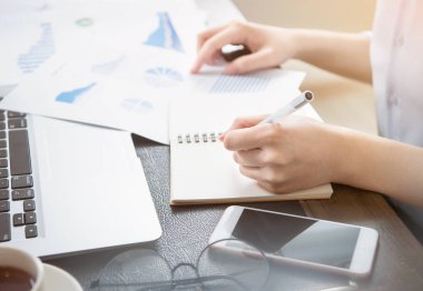İş konsepti. Kadın dizüstü bilgisayar ve ofis masasında rapor ile proje için not alır. Arka aydınlatma, güneş parlama etkisi, yakın, yan görünüm, kopyalama alanı