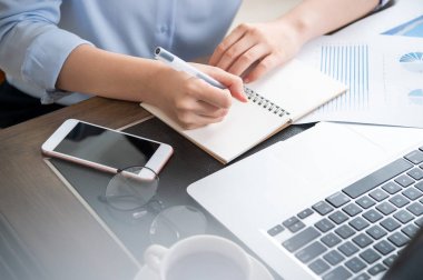 İş konsepti. Kadın dizüstü bilgisayar ve ofis masasında rapor ile proje için not alır. Arka aydınlatma, güneş parlama etkisi, yakın, yan görünüm, kopyalama alanı