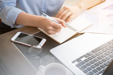 İş konsepti. Kadın dizüstü bilgisayar ve ofis masasında rapor ile proje için not alır. Arka aydınlatma, güneş parlama etkisi, yakın, yan görünüm, kopyalama alanı